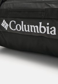 Zwarte reistas met Columbia-logo. Gemaakt van duurzaam materiaal, met sterke stiksels en een gladde textuur. Geaccentueerd met stevige handvatten.