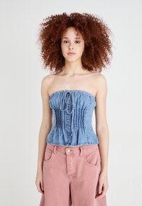 Top de ganga sem alças com corpete franzido, de cor azul-clara, e laço decorativo no decote. Combinado com calças largas rosas.