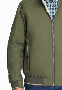 Chaqueta bomber verde oliva con cierre de cremallera, puños y dobladillo elásticos, que cuenta con bolsillos laterales y detalles de ribete en contraste.