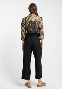 Wydrukowana, lekka bluzka w beżu i czerni, o luźnym kroju. Połączona z czarnymi, szerokimi spodniami i beżowymi butami wsuwanymi.