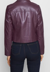 Veste cropped en cuir bordeaux avec une texture lisse, coutures d'épaule et points de couture propres, associée à un jean noir comportant deux poches arrière.