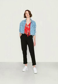 Jaqueta de denim azul claro sobre uma blusa floral vermelha com amarração, combinada com calças pretas ajustadas e ténis brancos. Texturas suaves e design casual.