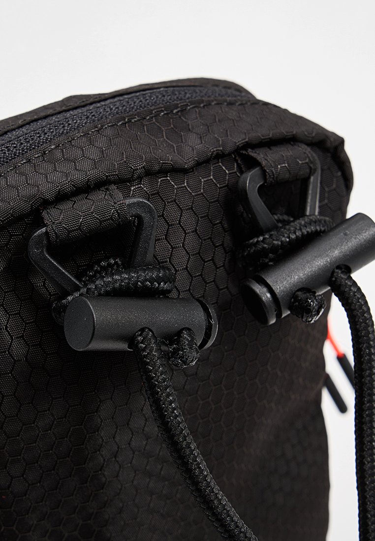 Schwarze Tasche mit hexagonalem Muster, ausgestattet mit schwarzen Kordelstoppern und Schnüren. Strapazierfähiges Material mit einer strukturierten Oberfläche. Naheaufnahme.