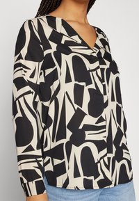 Blusa astratta nera e crema con scollatura a V e maniche lunghe; realizzata in tessuto liscio con una vestibilità comoda.