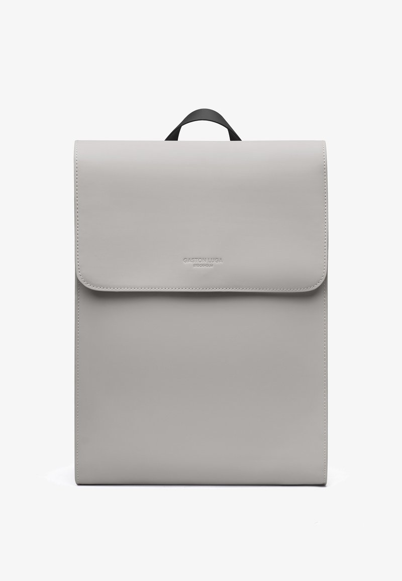 Minimalistischer rechteckiger Rucksack in hellgrau mit oberen Klappdeckel und kleinem schwarzem Griff, mit dezentem, eingeprägtem Markenlogo auf der Frontklappe.