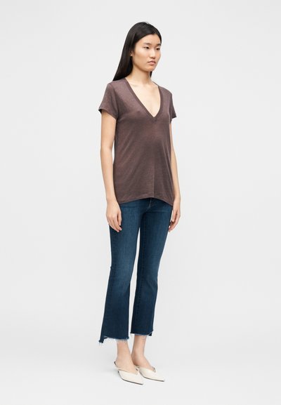 T-shirt castanha com decote em v e mangas curtas, usada com jeans cropped azul escuro com bainhas desfiadas e sapatilhas brancas pontiagudas.