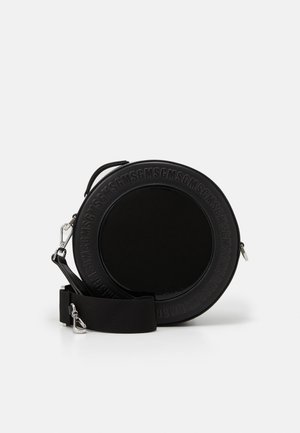 Okrągła czarna torba na ramię o błyszczącej powierzchni, z wytłoczonym tekstem na krawędzi, regulowanym paskiem i metalowymi elementami. Gładka faktura.