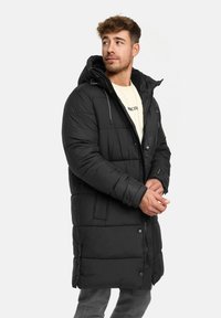 Zwarte gewatteerde lange jas met capuchon, voorzien van een ritssluiting aan de voorkant, drukknopen en zichtbare stiklijnen. Zachte textuur, geschikt voor koud weer.