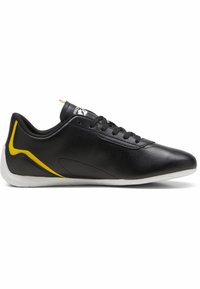 Černá sportovní bota s hladkým koženým svrškem, bílou podrážkou, žlutým akcentem na boku a černými tkaničkami. Navrženo pro výkon.
