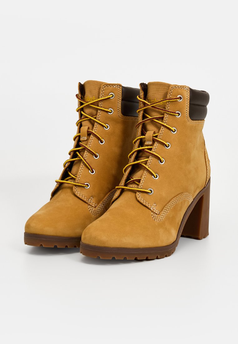 Stivaletti in suede marrone con tacco alto, lacci gialli e colletto imbottito marrone. Presentano cuciture decorative e suola in gomma testurizzata.