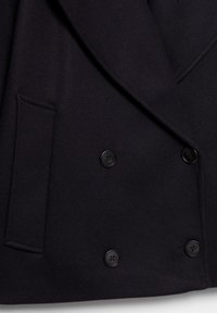 Manteau en laine noire à double boutonnage avec boutons noirs, col cranté et poches latérales. Texture lisse et détails de design structurés.