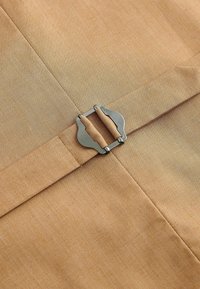 Tissu beige avec une boucle métallique servant de fermoir, reliant deux sangles de tissu superposées sur un vêtement ou un accessoire.