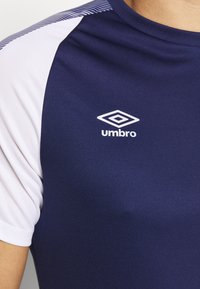 Námorně modré sportovní tričko s bílými rukávy, kulatým výstřihem a logem "Umbro" zobrazeným bílou barvou na části hrudi.