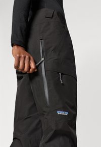 Μαύρο παντελόνι εξωτερικής χρήσης με δύο τσέπες με φερμουάρ, κατασκευασμένο από υλικό με υφή. Διαθέτει το λογότυπο της Patagonia και ρυθμιζόμενο κορδόνι στη μέση.
