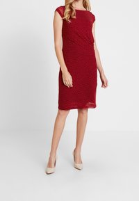 Rood jurkje met stippen, met korte mouwen, gedrapeerd ontwerp, knielange snit en een gladde textuur, gecombineerd met nude hoge hakken.