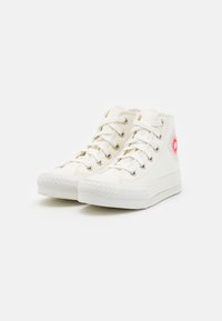 Zapatillas altas blancas de lona con un diseño de flores estampadas en el costado y suelas de goma blanca. Presentan ojales plateados y cordones.