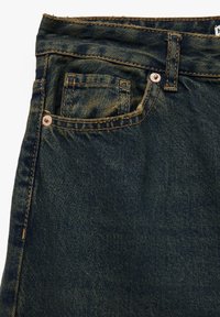 Los jeans de mezclilla oscura presentan un diseño de cinco bolsillos, costuras en contraste y un borde desgastado en la cintura para añadir textura.