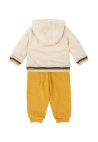 Sudadera beige con capucha, con dobladillo acanalado y detalles en azul marino y amarillo, combinada con pantalones de chándal amarillos de tejido suave y puños elásticos.