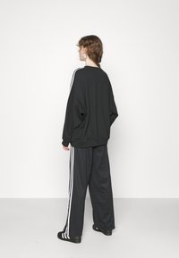Felpa oversize nera con strisce verticali bianche sulle maniche, abbinata a pantaloni neri a gamba larga con accenti a striscia.