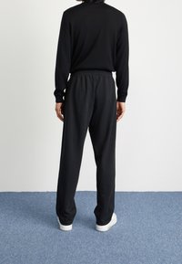 Svart långärmad topp och matchande byxor med resår i midjan, tillverkade av mjukt tyg. Modellen bär vita sneakers. Bakifrån.