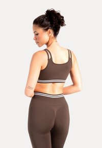 Sujetador deportivo marrón con doble tirante y banda con rayas blancas, combinado con leggings marrones a juego que muestran una textura suave y un diseño ajustado.