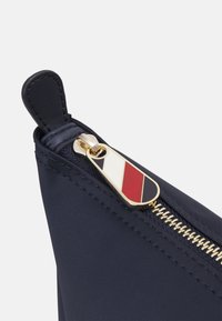 Gros plan d'une pochette en tissu bleu marine avec une fermeture éclair dorée et un onglet présentant un motif rayé diagonal rouge, blanc et noir.