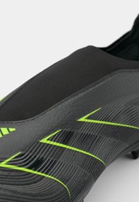Zwarte voetbalschoen met groene accenten, gladde synthetische bovenkant, gestructureerde details, en een gestroomlijnd ontwerp. Gepunte buitenzool voor grip.