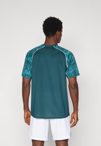 Tume teal värvi lühikeste varrukatega spordijacket. Omab tekstureeritud selga ja mustritega õlavarrepaneele heledama teal värviga. Lameõmblused.