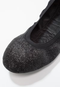 Gros plan d'une ballerine noire pailletée avec un bout arrondi et une bordure élastique autour de l'ouverture.