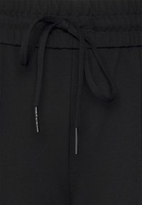 Schwarze Jogginghosen mit einem elastischen Bund, ausgestattet mit einem flachen Kordelzug und glatter Textur. Einfaches Design ohne sichtbare Muster oder Akzente.