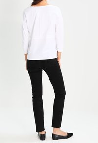 Vit långärmad topp med vid halsringning, med en sömdetalj på baksidan. Matchad med figurnära svarta jeans och svarta lägenheter.