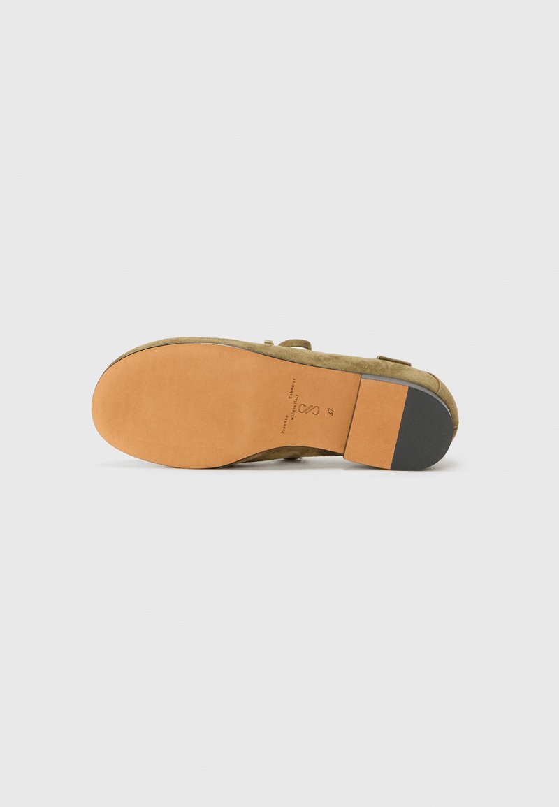 Suede slip-on shoe with a beige upper. Features a tan rubber sole with a black accent and subtle branding on the heel. Round toe design.
