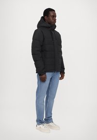 Black puffer jacket with a hood, featuring a quilted design and front zip closure. Paired with light blue jeans and white sneakers.