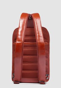 Mochila texturizada roja con correas acolchadas, cierre de cremallera y detalles en cuero suave. Presenta un diseño estructurado con un bolsillo lateral con cremallera.