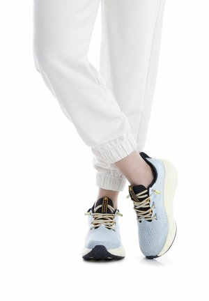 Zapatillas deportivas azul claro con detalles en negro, parte superior de malla transpirable, suela blanca gruesa y cordones amarillos, sobre un fondo liso.