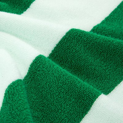 Primo piano di tessuto morbido e strutturato con strisce orizzontali verdi e bianche, che mostra anelli intrecciati e pieghe di un asciugamano o coperta.