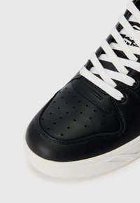 Μαύρο δερμάτινο sneaker με περφοραρισμένο μπροστινό μέρος, λευκά κορδόνια και λευκή καουτσούκ σόλα. Λειαντική υφή με διακριτικές ραφές.