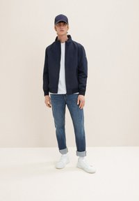 Chaqueta de bombardero navy con cierre frontal, camiseta blanca de cuello redondo, jeans azules, puños enrollados y zapatillas blancas. Diseño simple y tejido ligero.
