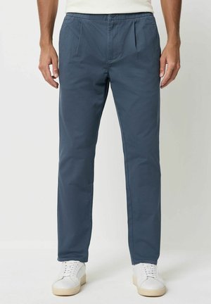 Herren navyblaue Hosen aus glattem, leichtem Stoff. Mit Falten, Knopfverschluss und schmalem Bein-Design. Kombiniert mit weißen Sneakers.