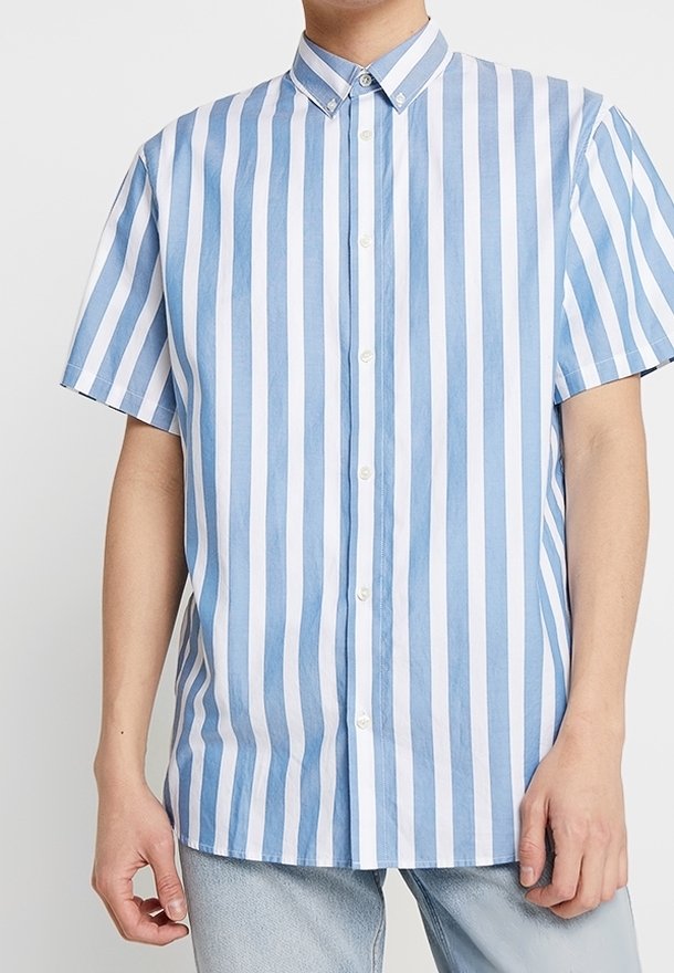 Camicia a manica corta con bottoni, a righe verticali blu chiaro e bianche, colletto a punta e vestibilità rilassata. Realizzata in un tessuto leggero.