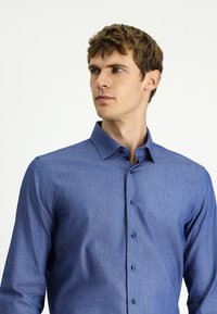 Niebieska koszula z długim rękawem, zapinana na guziki, wykonana z teksturowanej tkaniny, z wysuniętym kołnierzykiem i z przodu zapinana na guziki, z delikatnym wzorem na całej powierzchni.