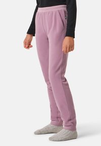 Pantaloni in pile color lilla pastello, con vita a coste e tasche laterali, vestibilità affusolata con polsini a costine, indossati con calzini grigi lavorati a maglia.