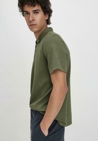 Olijfgroene polo met zachte stof, heeft een klassieke kraag en korte mouwen, met een subtiele logo op de linkerschouder.