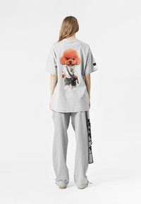 Camiseta gris de gran tamaño con un gráfico de un perro de dibujos animados en un traje de karate en la parte de atrás. Combinada con pantalones de chándal gris claro y acentos negros.