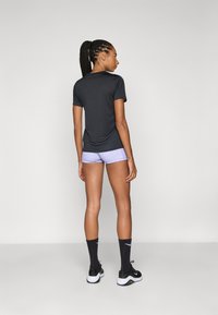Black short-sleeve athletic shirt paired with light purple shorts. Model wears black socks and black athletic shoes, showing a streamlined design.