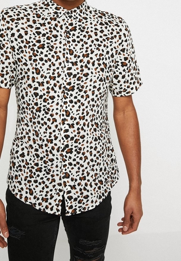 Camicia a maniche corte in tessuto bianco con stampa leopardata nera e marrone, dotata di colletto a punta e chiusura con bottoni frontali.
