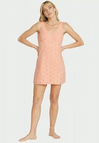 Φόρεμα σε ροδακινί χρώμα χωρίς μανίκια, φτιαγμένο από δαντέλα με ανθισμένες κοπές, διαθέτει V-λαιμόκοψη και εφαρμοστό κορσέ, με φουσκωτό φούστα.