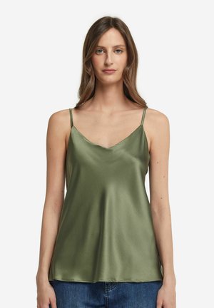 Camisola in satin verde oliva con spalline sottili e scollatura a V. Texture liscia con un morbido drappeggio. Indossata con pantaloni in denim casual.