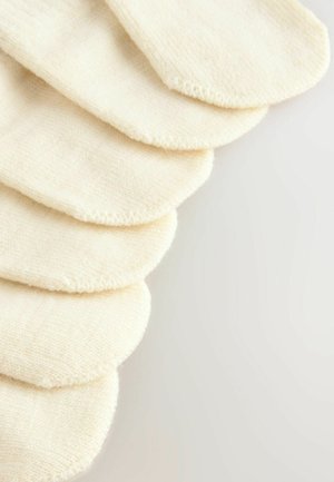 Chaussettes en coton crème disposées en tas, présentant une texture lisse et un renforcement le long des bords.