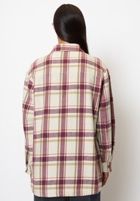 Flannel shirt in cream, maroon, and olive plaid pattern. Features a collar, button cuffs, and a relaxed fit with a straight hem.